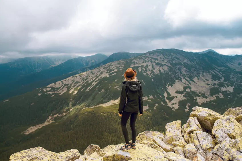 Kvinna står uppe på ett berg och tittar på utsikten. Foto.