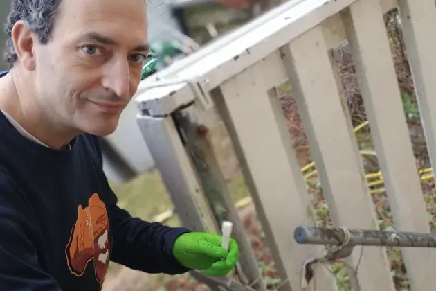 Forskare ser in i kameran, håller i ett provrör. Foto.