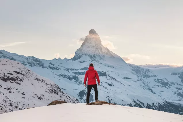 En person står uppe på ett berg och tittar ut över ett snötäckt landskap. Foto.