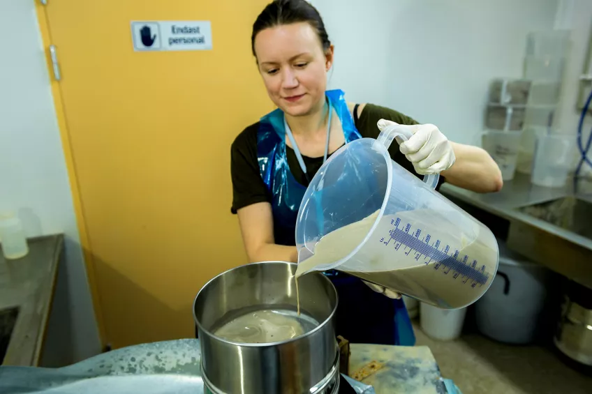 En kvinna blandar material i en behållare i ett labb. Foto.